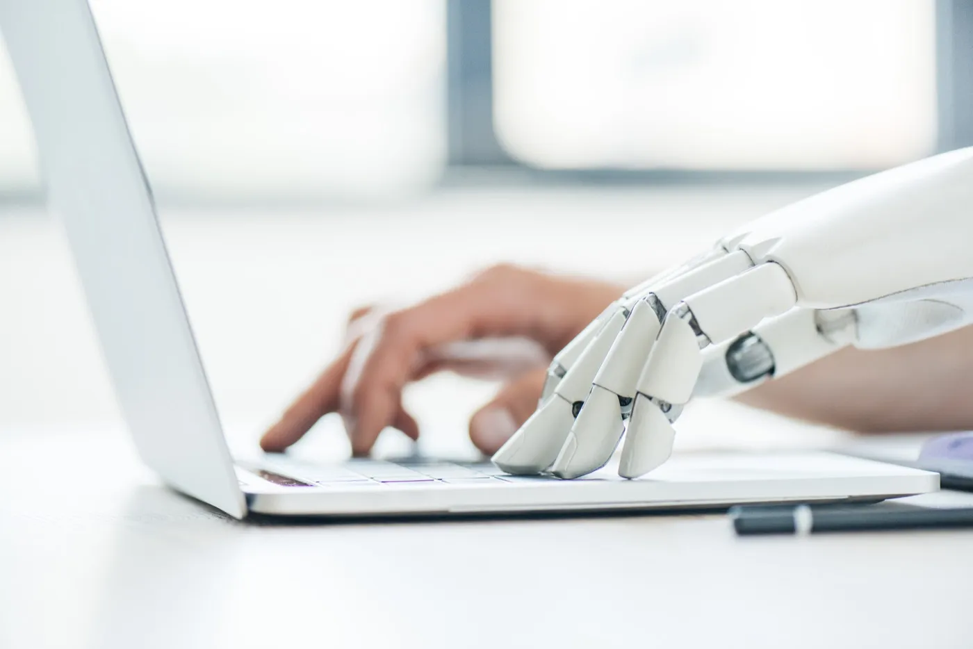 Manos humanas y robóticas trabajando en el teclado de un portátil